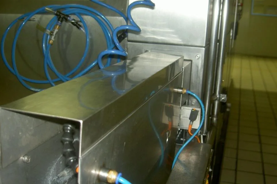 Stainless steel aseptic filling equipment with pneumatic tubing and sensors on a tiled plant floor.