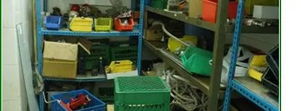 Spare parts shelving with mixed boxes, loose components, and crates stacked without order.